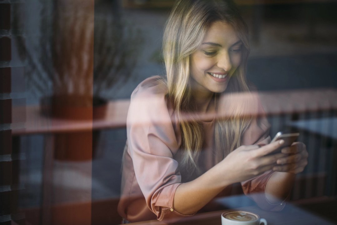 Lächelnde Frau tippt im Café auf ihrem Smartphone