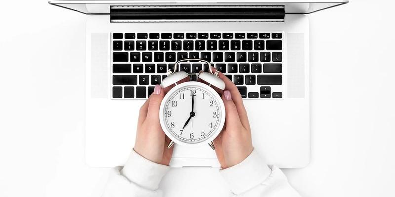 Hände halten einen Wecker über einer Laptop-Tastatur