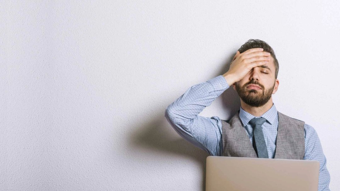 Mann fasst sich genervt an die Stirn, vor ihm ein Laptop