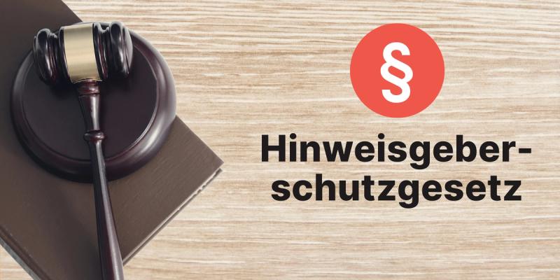 Richterhammer auf einem Gesetzbuch neben Paragrafenzeichen und Schriftzug Hinweisgeberschutzgesetz