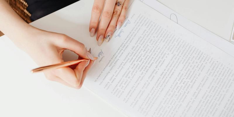 Hand unterschreibt mit einem Stift ein mehrseitiges Vertragsdokument