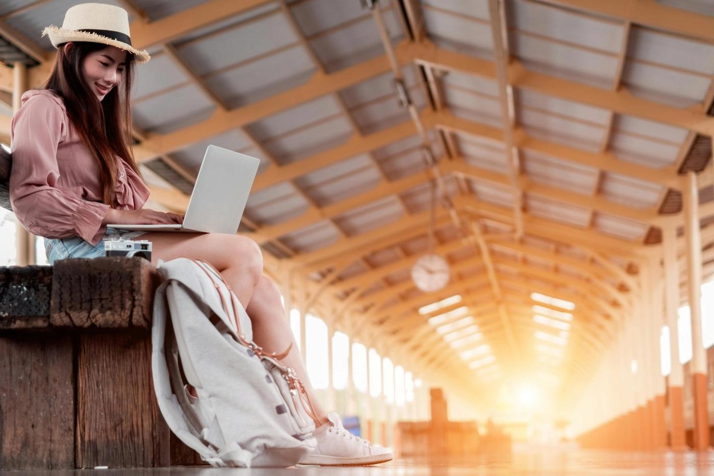 Frau mit Hut arbeitet am Laptop auf einem Bahnsteig