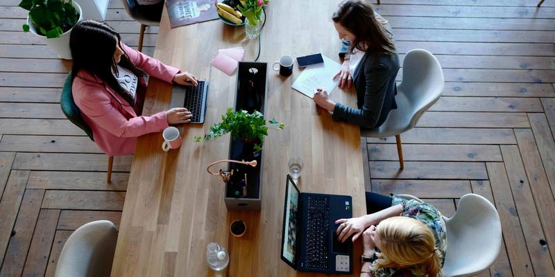 Draufsicht auf einen langen Gemeinschaftstisch, an dem mehrere Personen an Laptops arbeiten