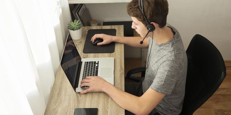 Person mit Headset arbeitet zu Hause am Laptop im Remote Work