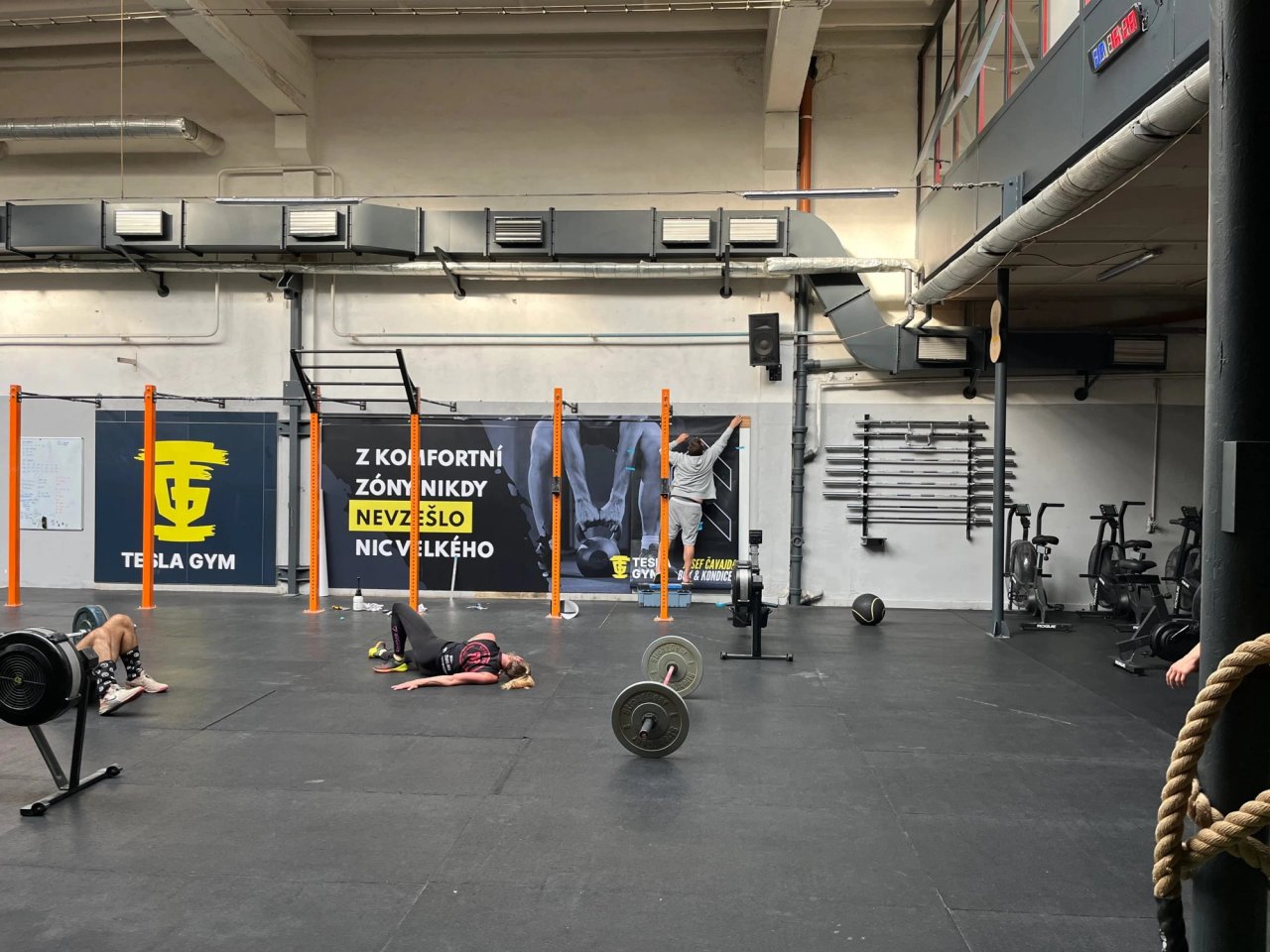 Sál Tesla gym s činkami a motivačním plakátem na stěně