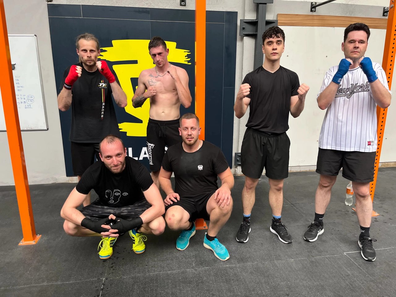 Skupina cvičenců s trenérem před logem Tesla gym
