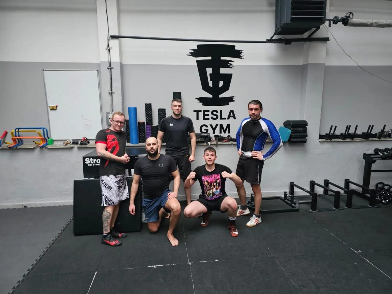 Skupina sportovců pózuje před velkým logem Tesla gym