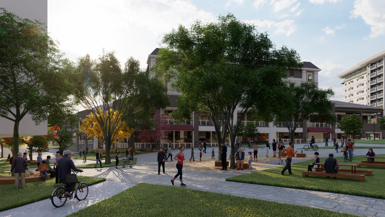 Rendered image of a public plaza in the late afternoon, with people walking, sitting, biking, and socializing among trees and benches. Sunlight filters through the leafy green and yellow trees, creating a warm, welcoming atmosphere. In the background are multi-story buildings with balconies, giving the space a campus or mixed-use community feel.