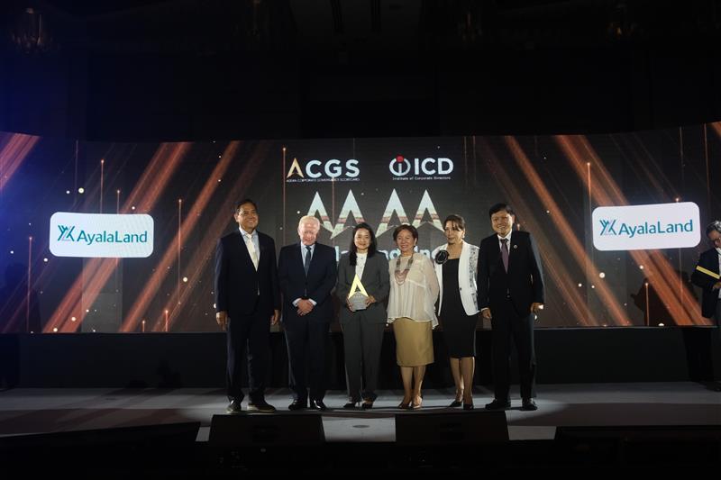 A group of six formally dressed individuals pose on stage during a corporate event, with logos of Ayala Land, ACGS, and ICD displayed on a large screen behind them.