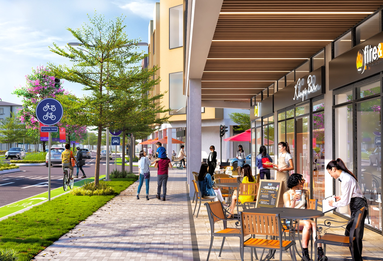Vibrant street-level view of a mixed-use development featuring outdoor dining, retail shops, tree-lined walkways, bike lanes, and pedestrians enjoying a lively, walkable environment under sunny skies.