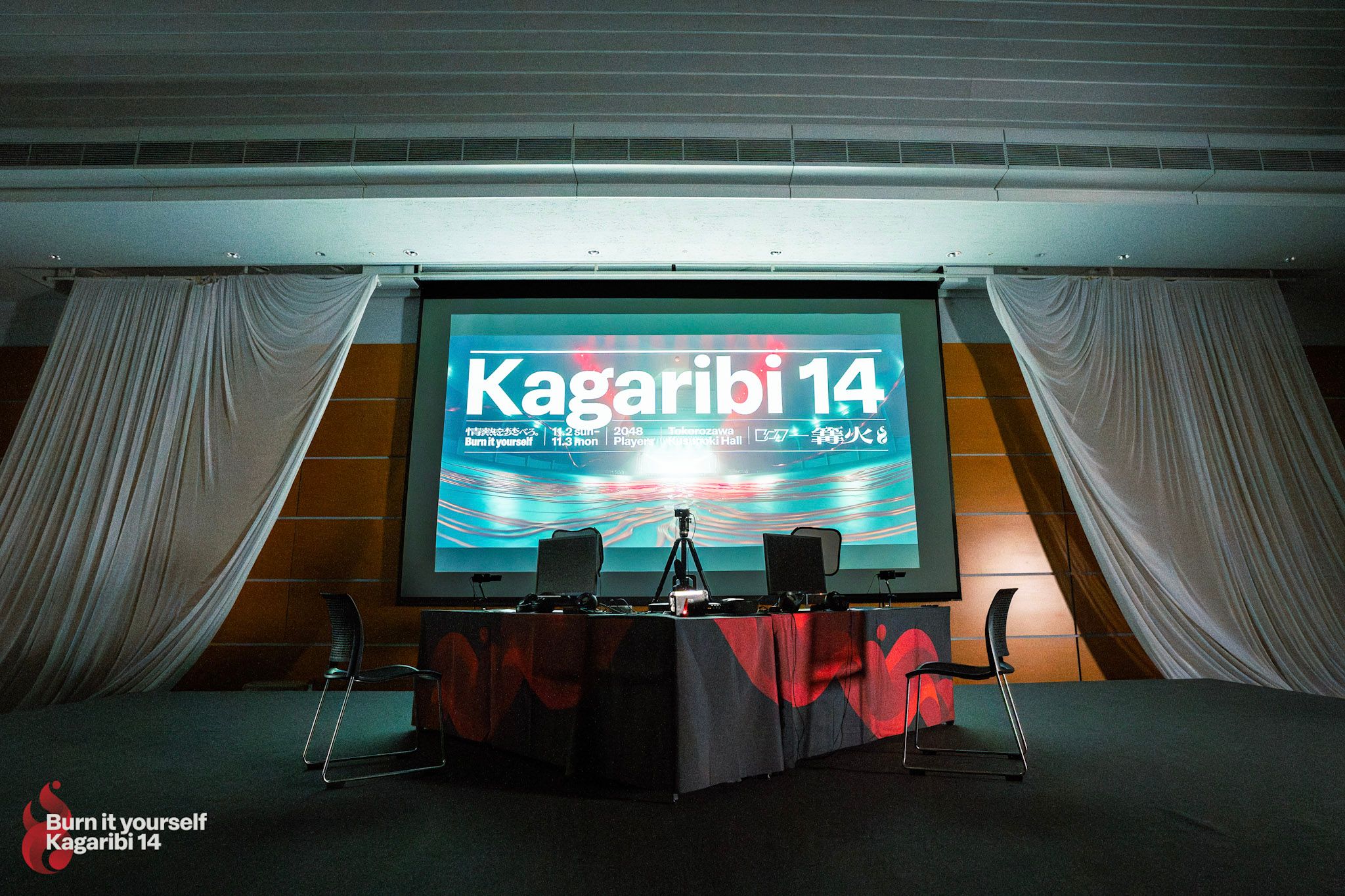 くすのきホールのメイン対戦台と、スクリーンに映し出されたオープニングの1カット。