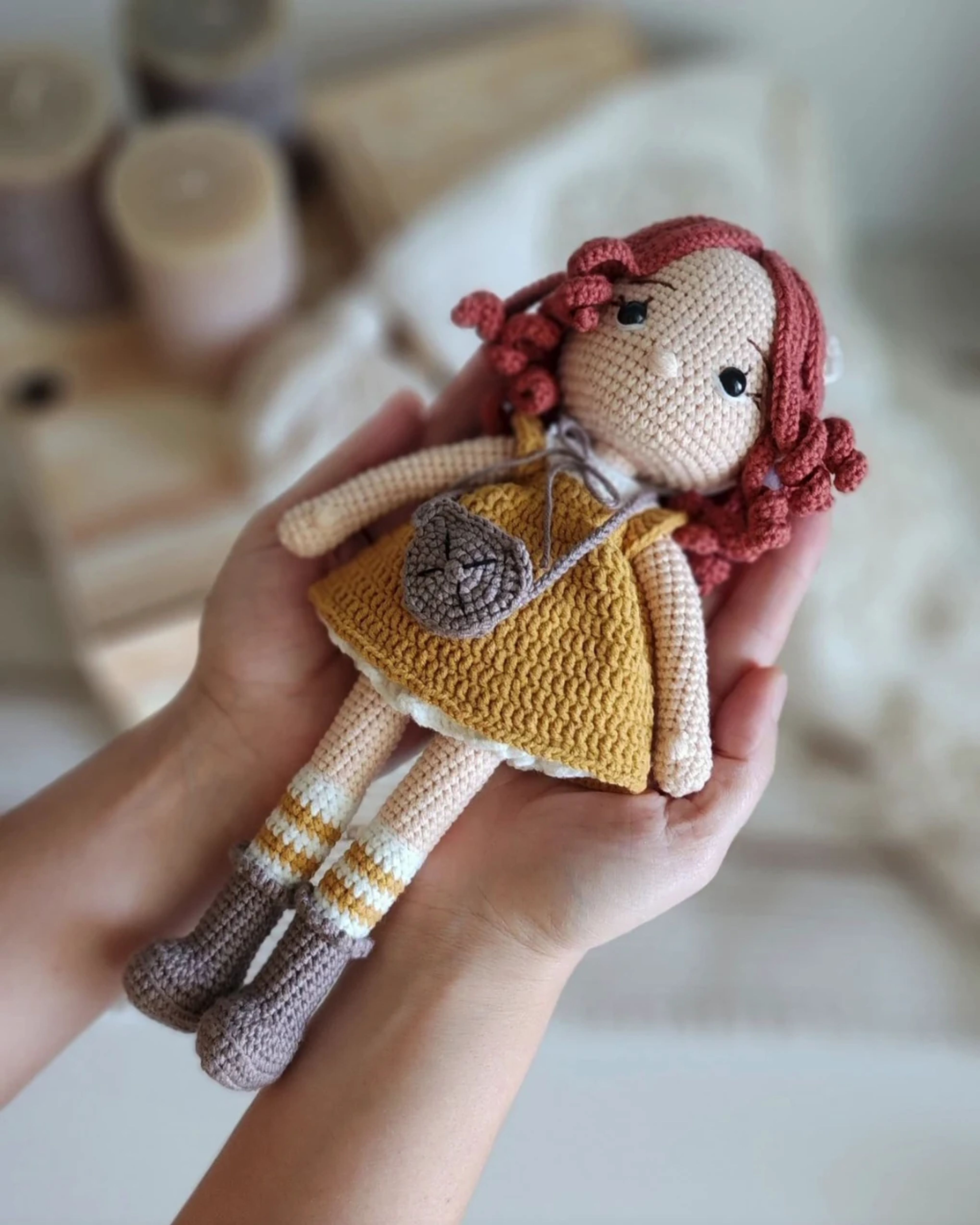 Crochet doll with red hair and a mustard dress held in two hands