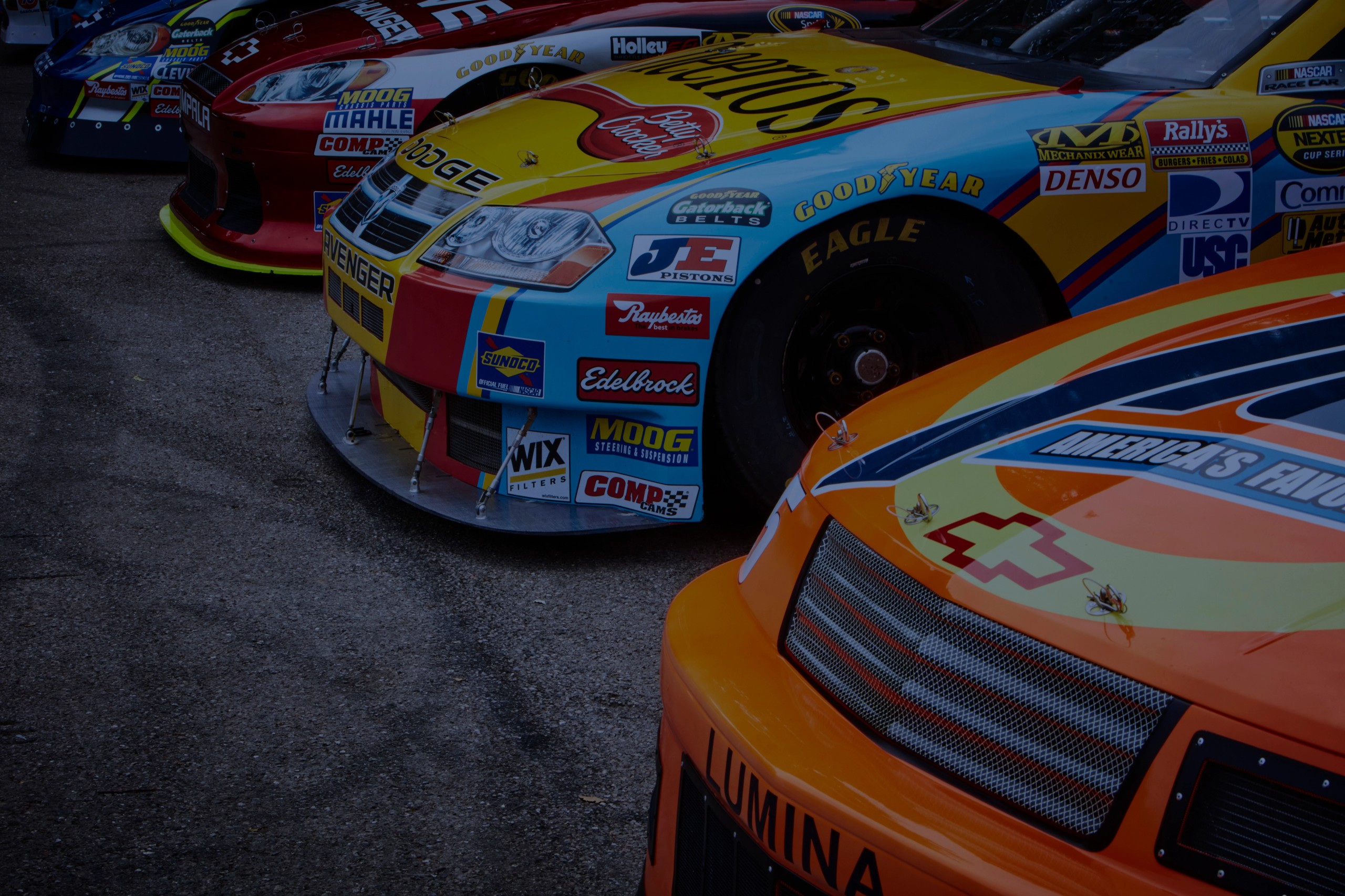 Colorful front ends of multiple NASCAR race cars displaying sponsor logos.