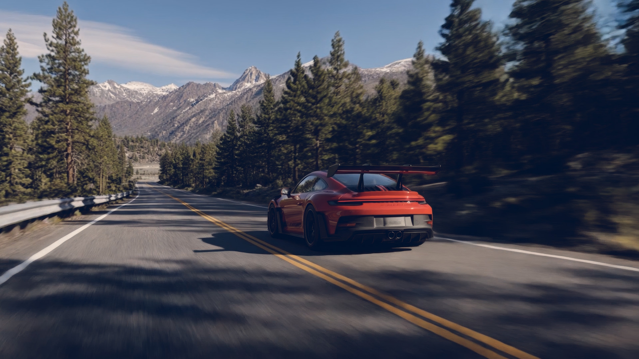 Modern performance car driving along a mountain road surrounded by pine forest.