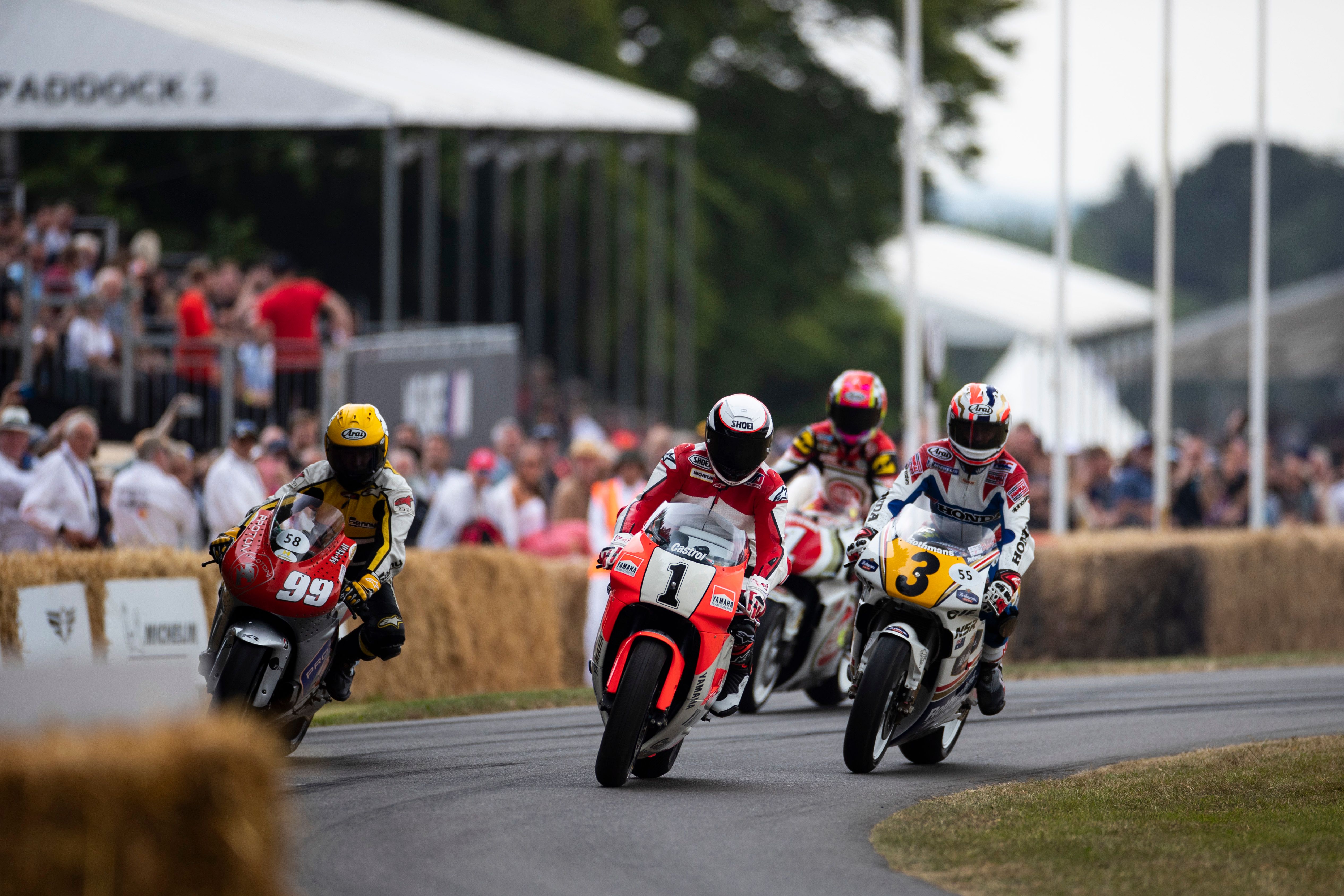 Motorcyclists race around a bend on a track lined with hay bales and spectators.