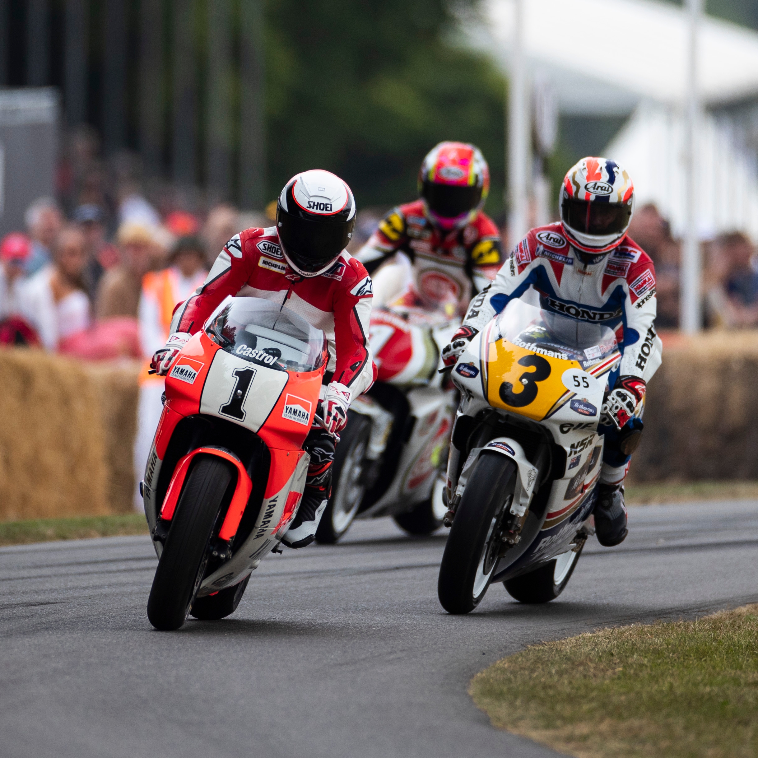 Motorcyclists race around a bend on a track lined with hay bales and spectators.