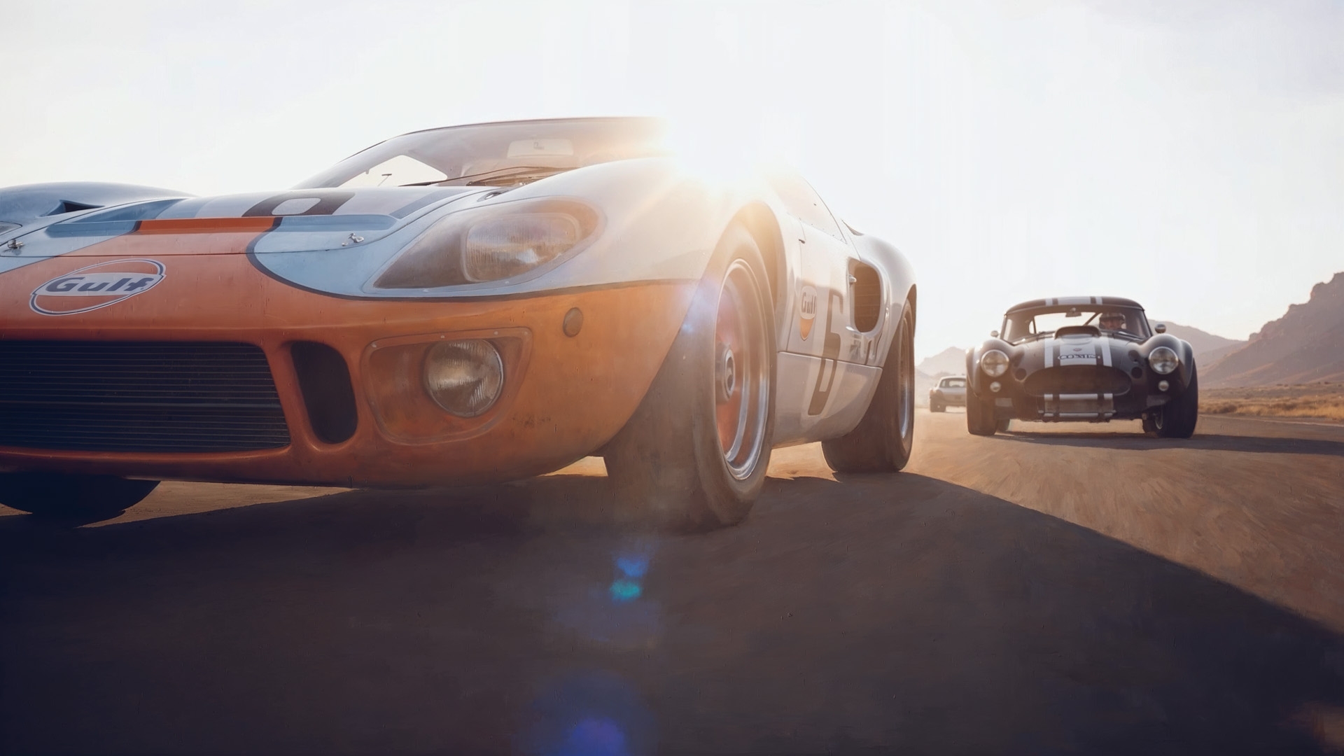 Historic racing cars driving at speed across an open desert road.