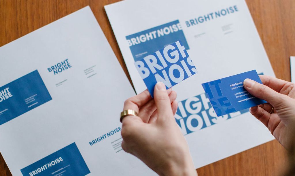 A woman is shown reviewing business card designs. Only her hands are visible as she holds the cards.