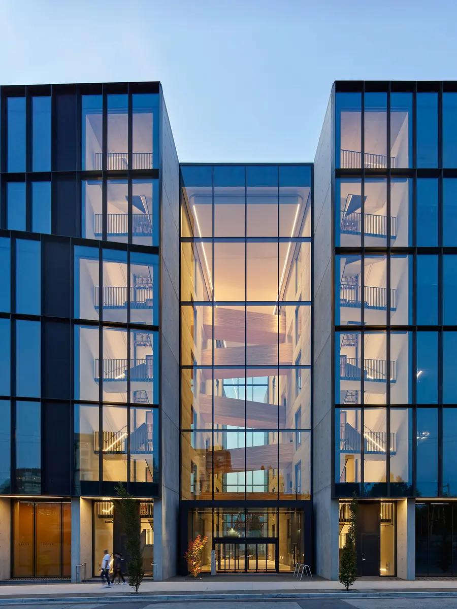 A modern, glass building with interior lighting showcasing an interior wooden staircase