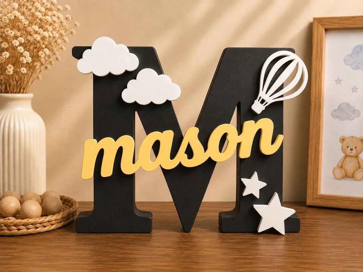 A freestanding 3D printed name sign decorated with small shapes, standing on a shelf in a child's room.