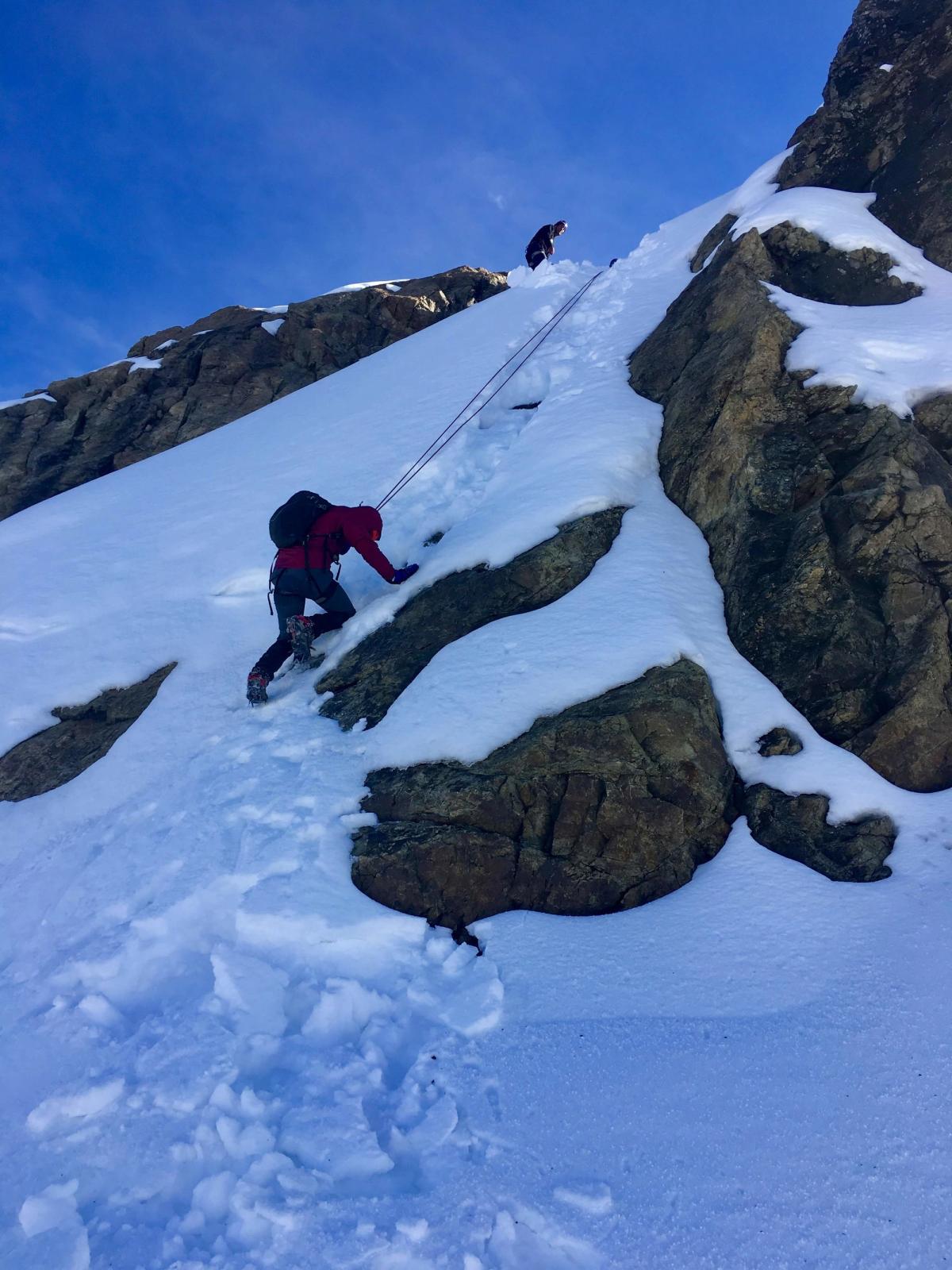 Climbing down a small snowfield with rope and an ice pick
