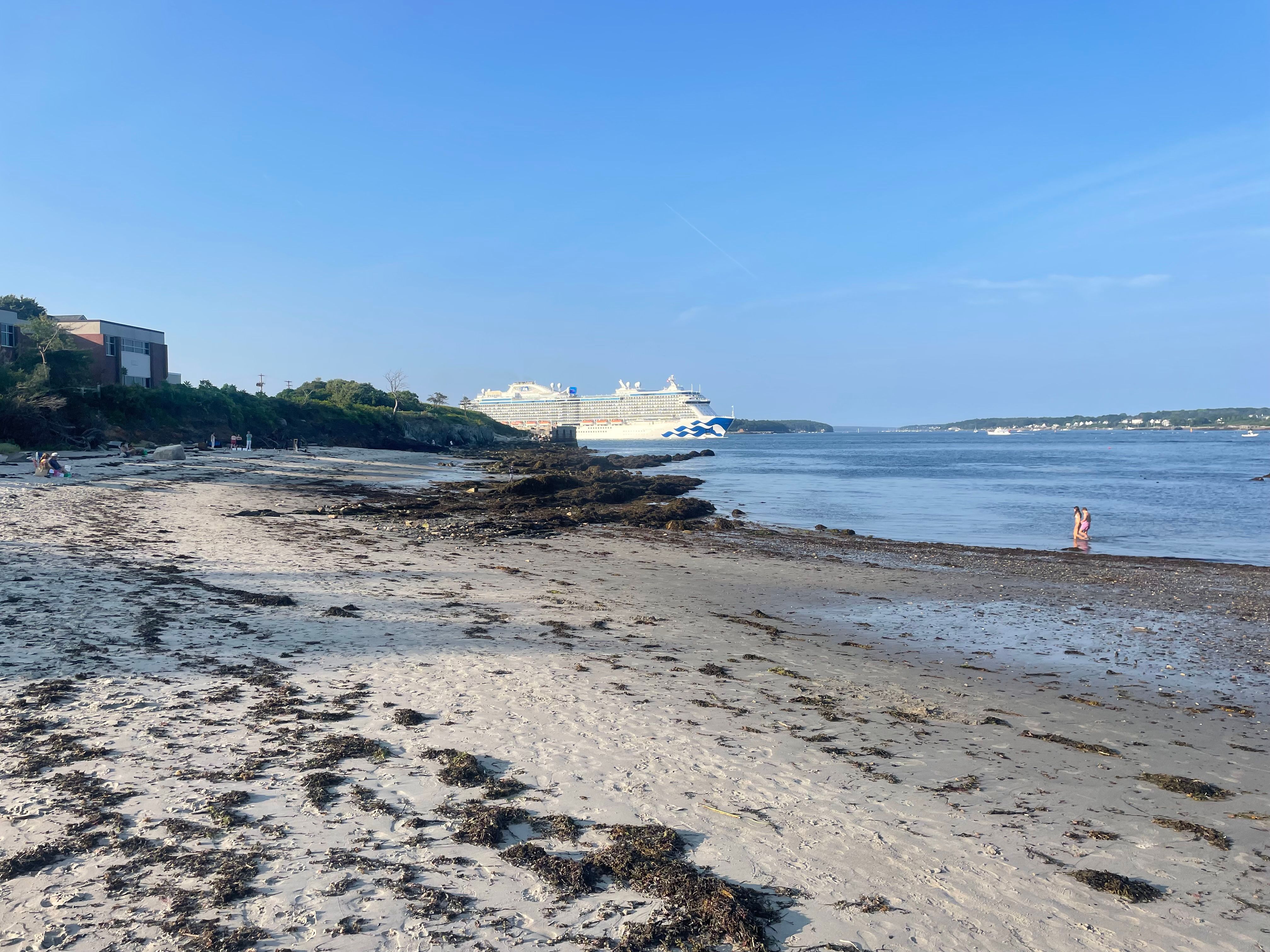 Sandy beach at low tide in Portland, Maine, with a large cruise ship docked across the harbor