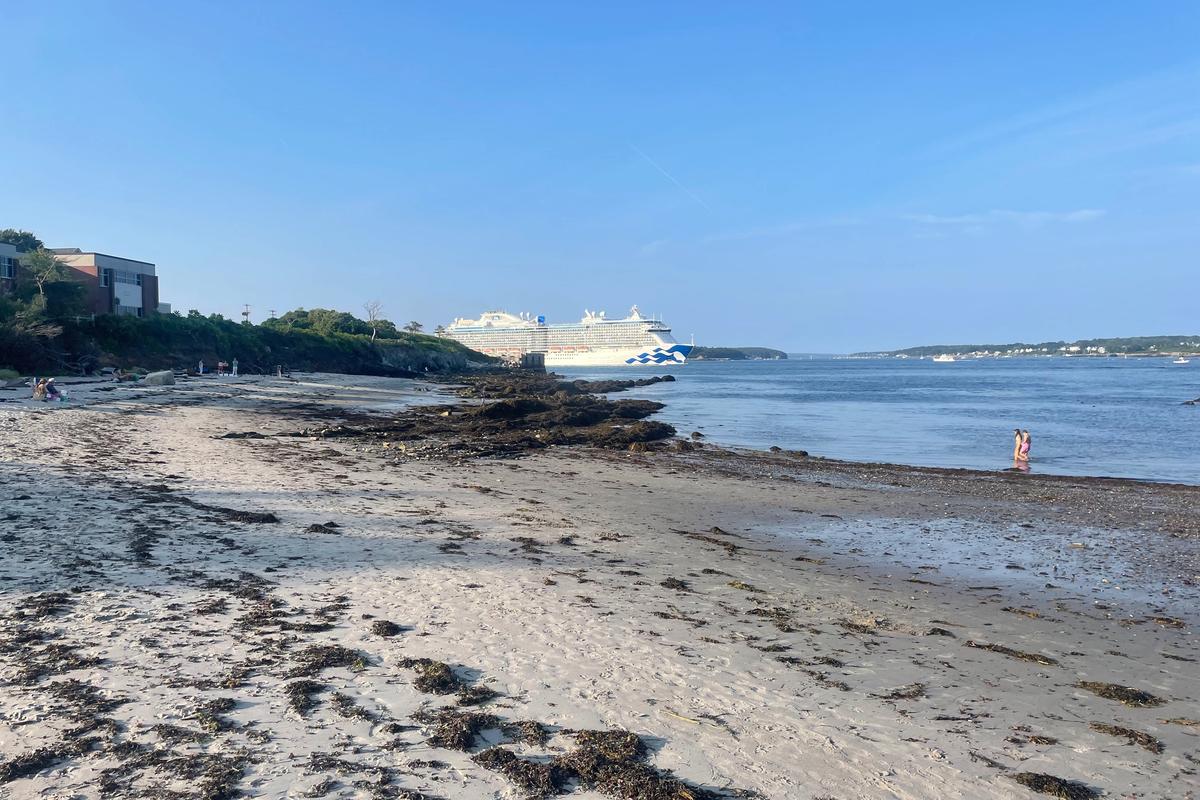 Sandy beach at low tide in Portland, Maine, with a large cruise ship docked across the harbor