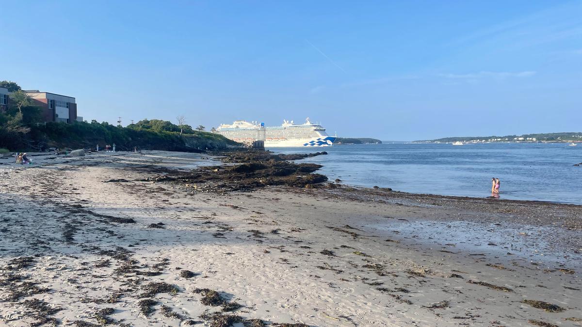 Sandy beach at low tide in Portland, Maine, with a large cruise ship docked across the harbor