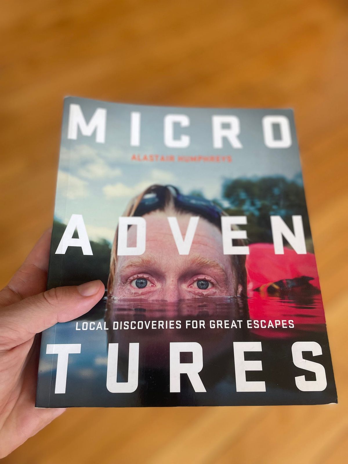 Hand holding a copy of the book Microadventures by Alastair Humphreys