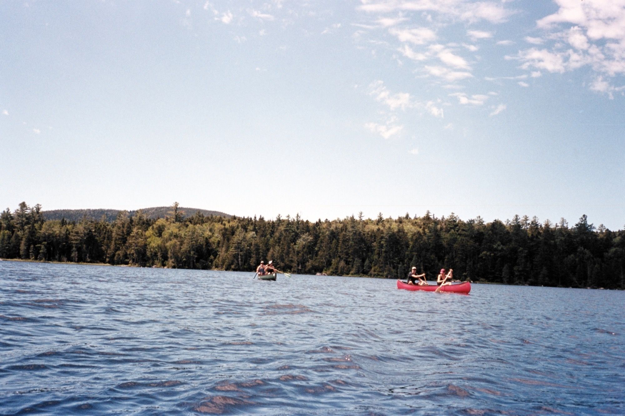 Two red canoes paddling across a blue Maine lake lined with forest