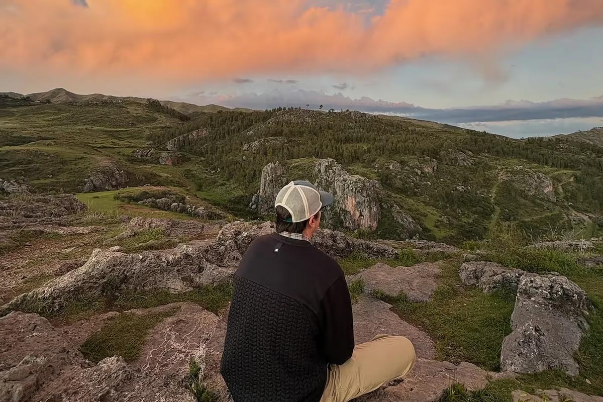 Man sitting on a rocky hilltop looking out over green hills at sunset