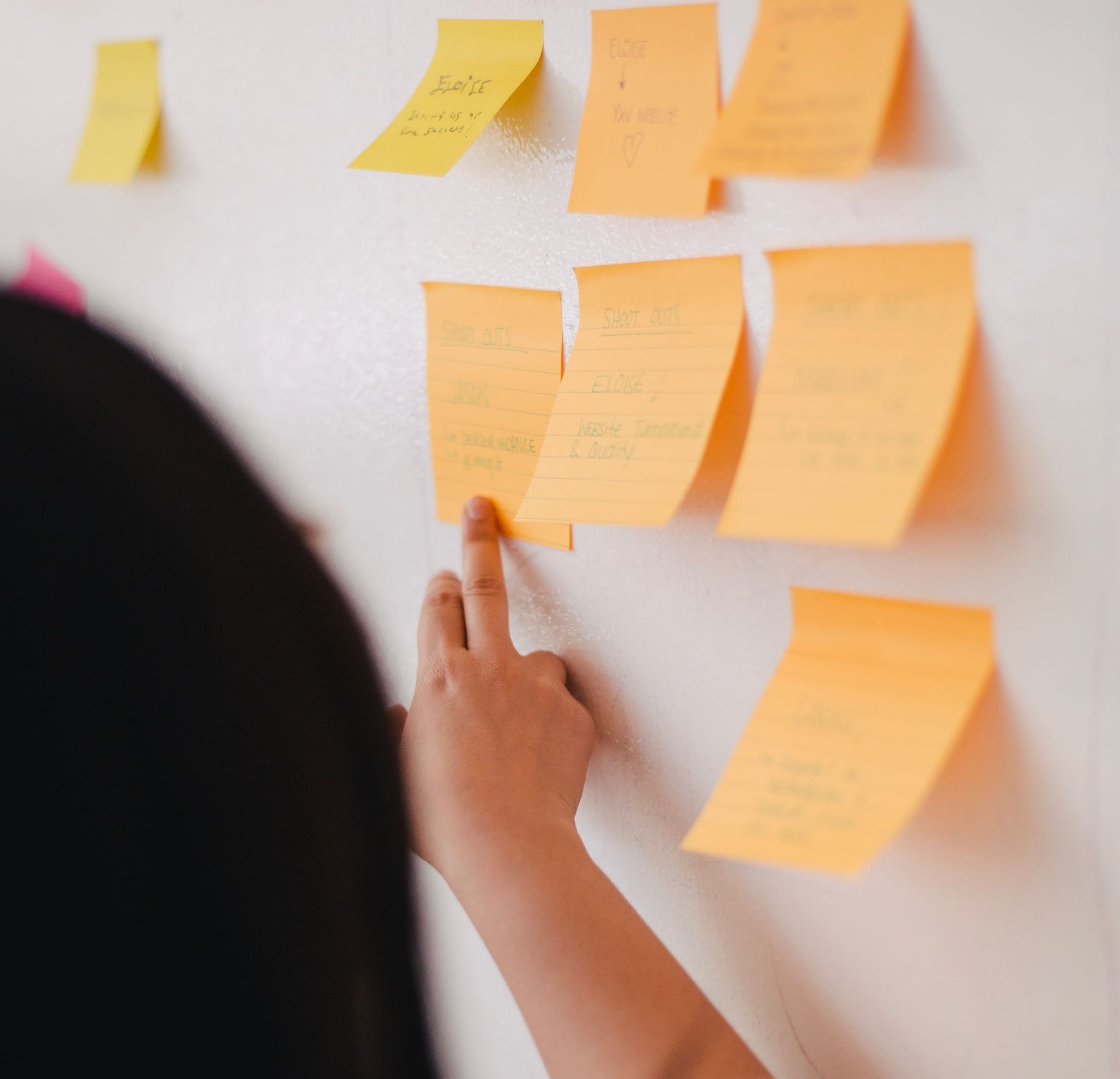 Hand placing orange sticky notes on a white wall