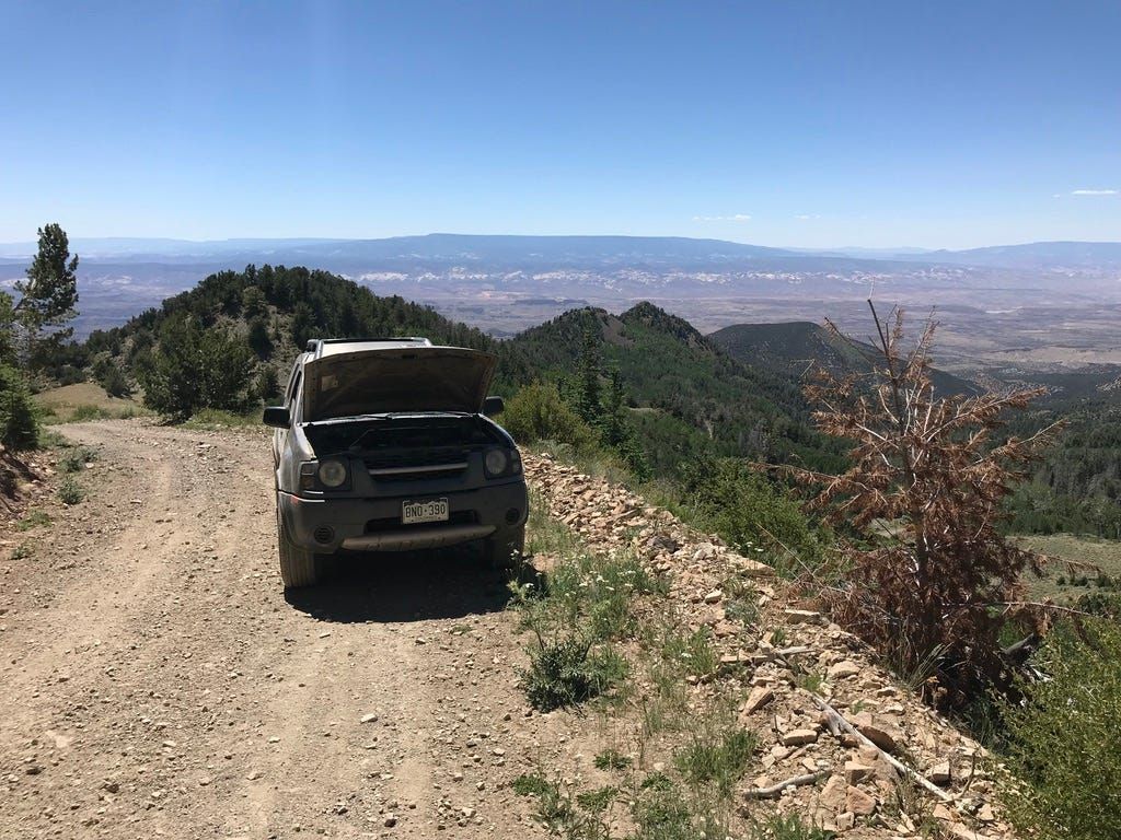 Pickup truck with its hood up on a remote dirt road overlooking desert mesas