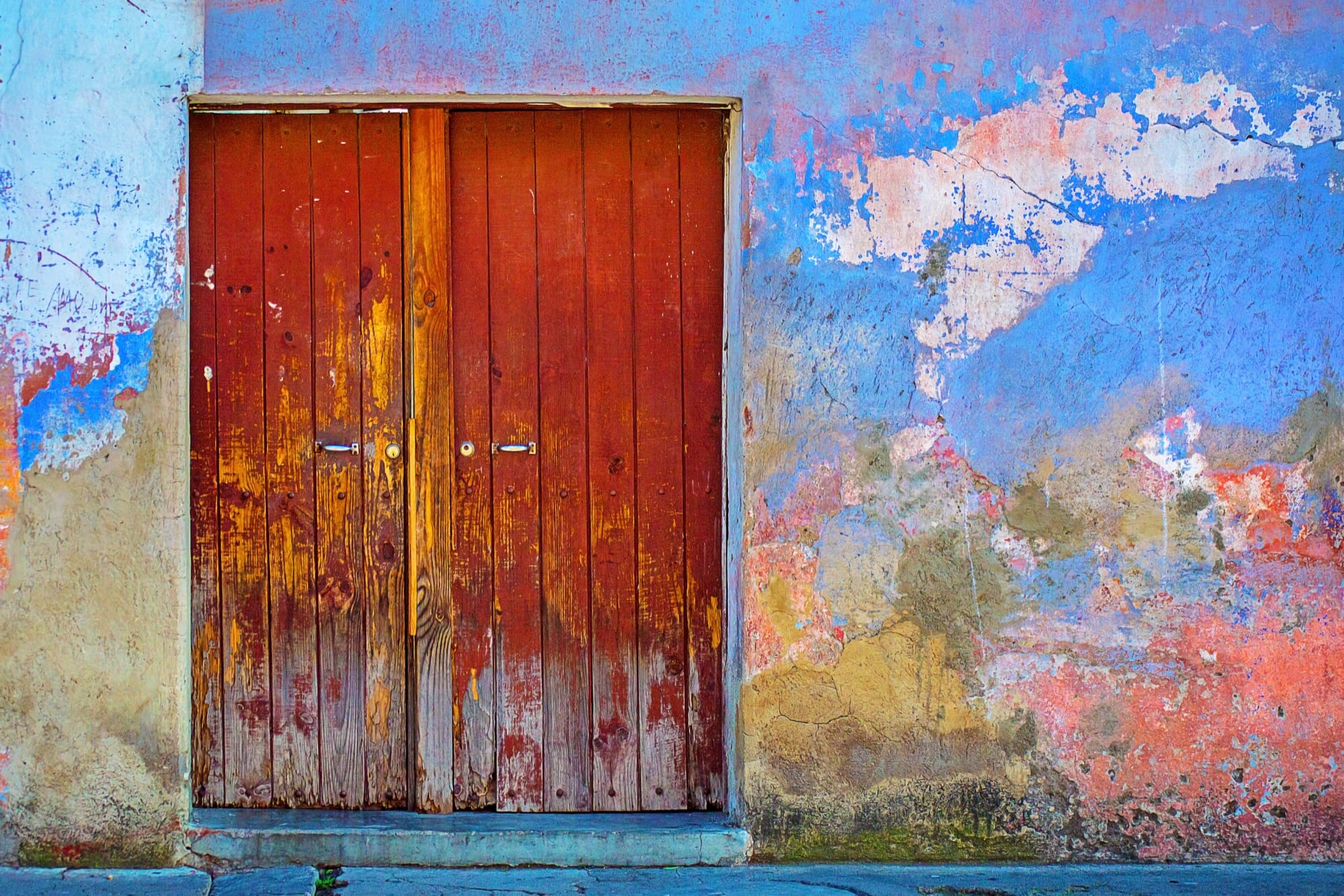Weathered red wooden doors set in a peeling blue and orange wall