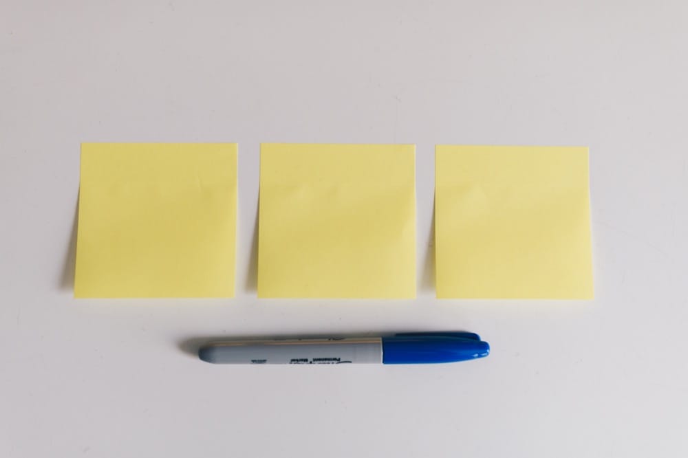 Three blank yellow sticky notes and a blue marker on a white surface