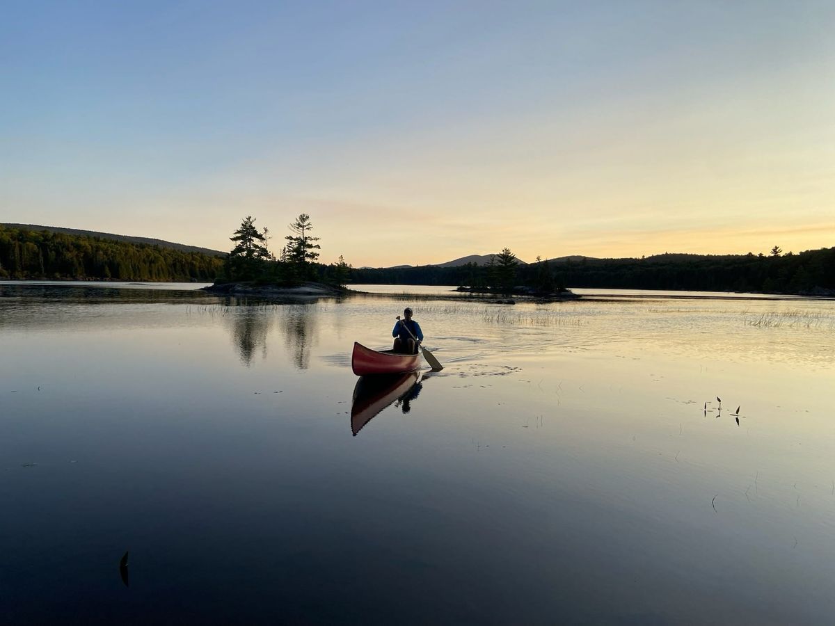 Person paddling a red canoe across a still lake at sunset