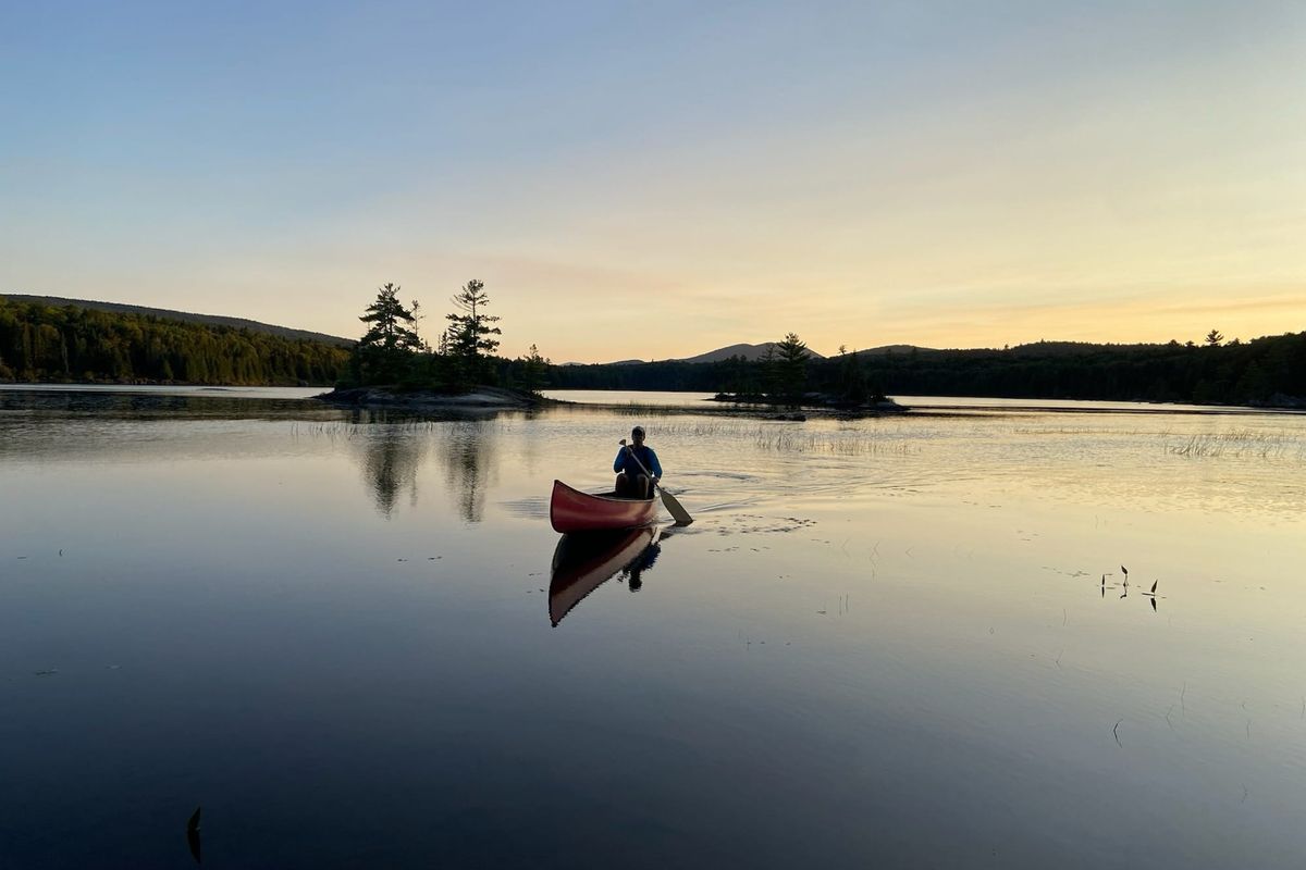 Person paddling a red canoe across a still lake at sunset