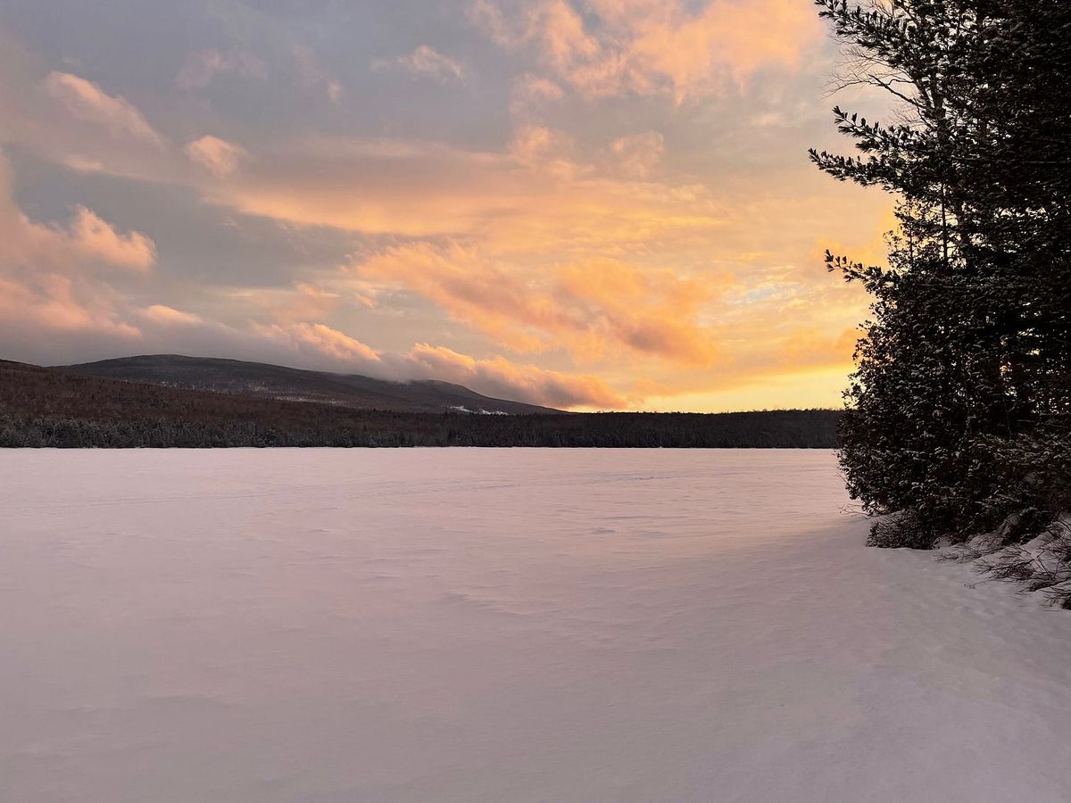 Snow-covered frozen lake under a pink and orange sunset sky