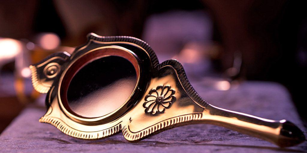 a brass hand mirror with a flower on it is sitting on a table .