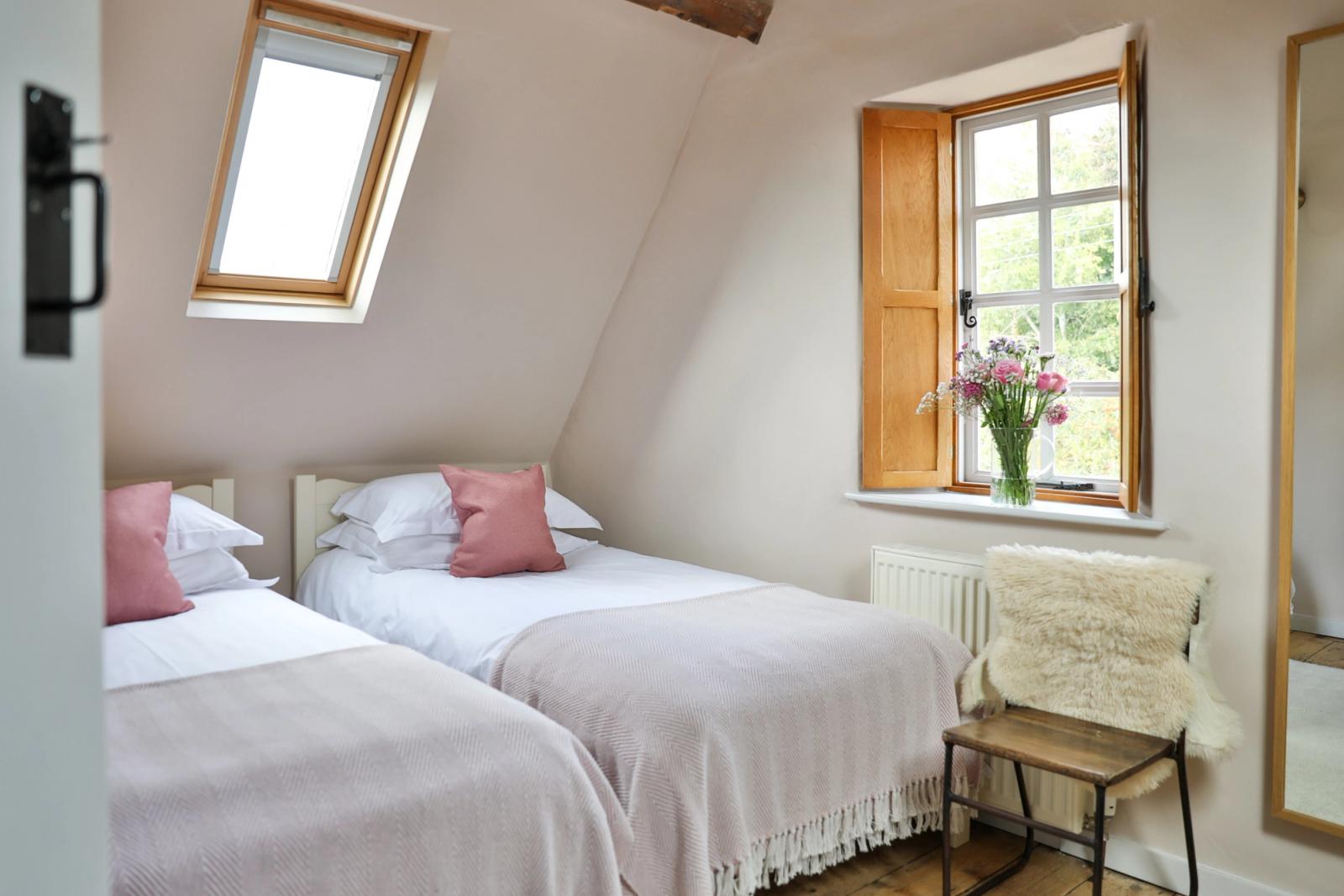 Bedroom with twin beds, pink scatter cushions, skylights, and natural light
