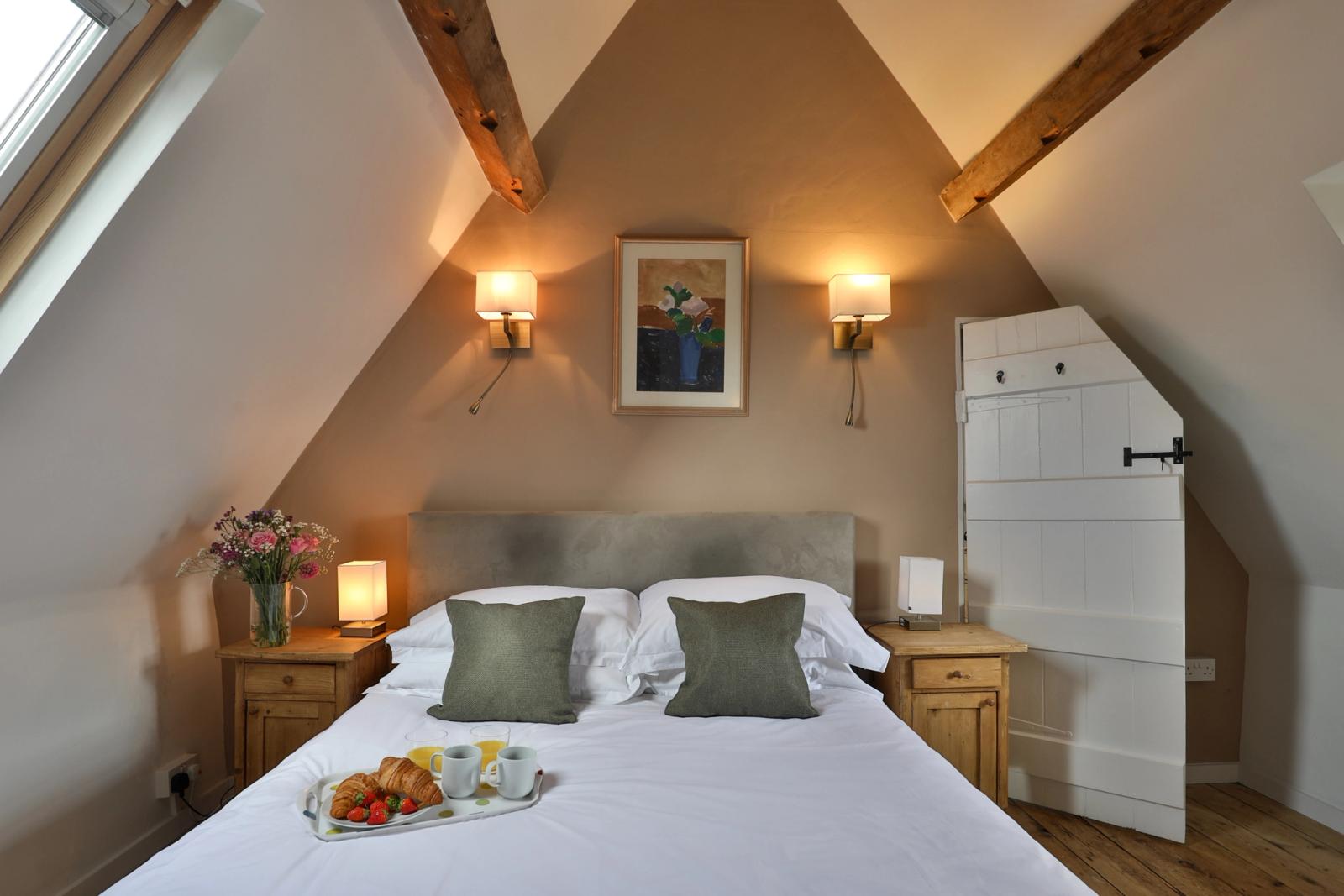 Bedroom with white bed, exposed wooden beams, warm lighting, and cream walls