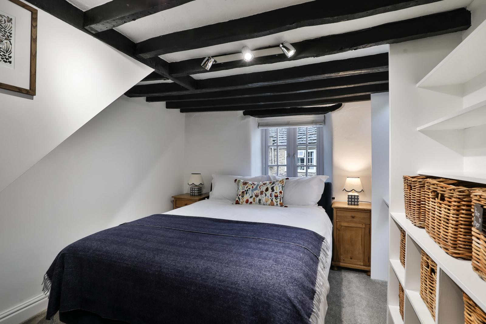 Bedroom with dark blue bed, exposed black beam, wooden furniture, and shelving