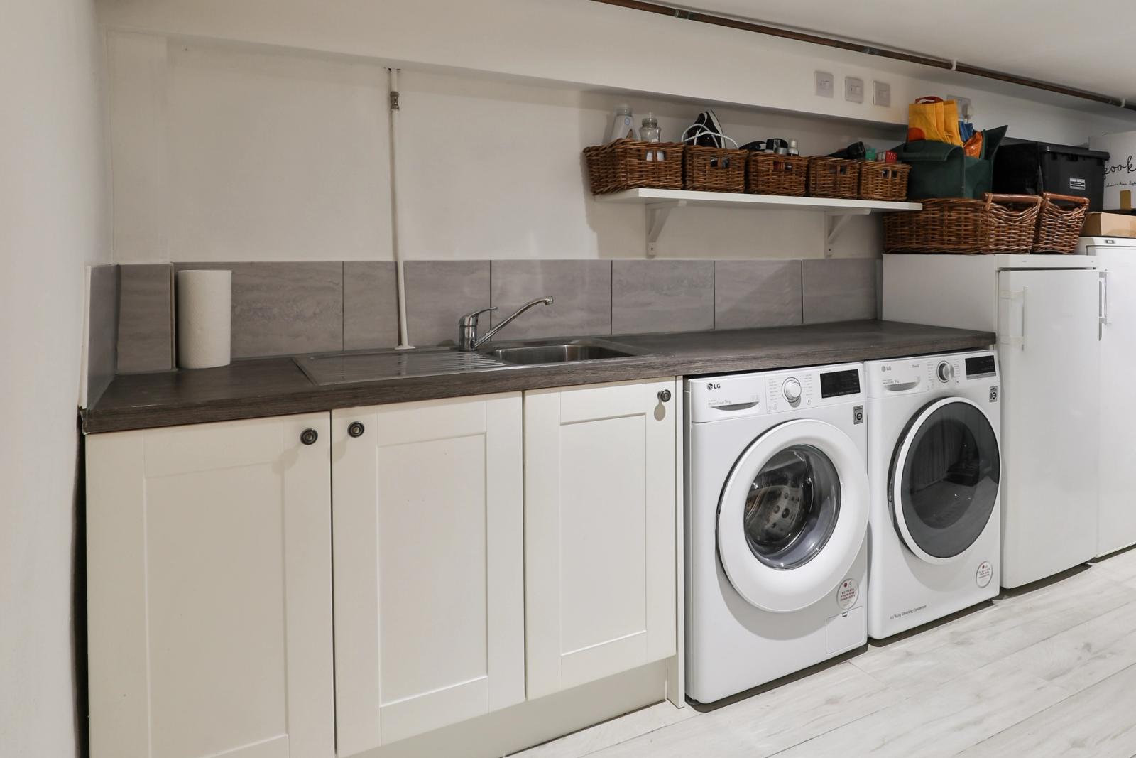 Laundry room with white cabinetry, two washing machines, and countertops