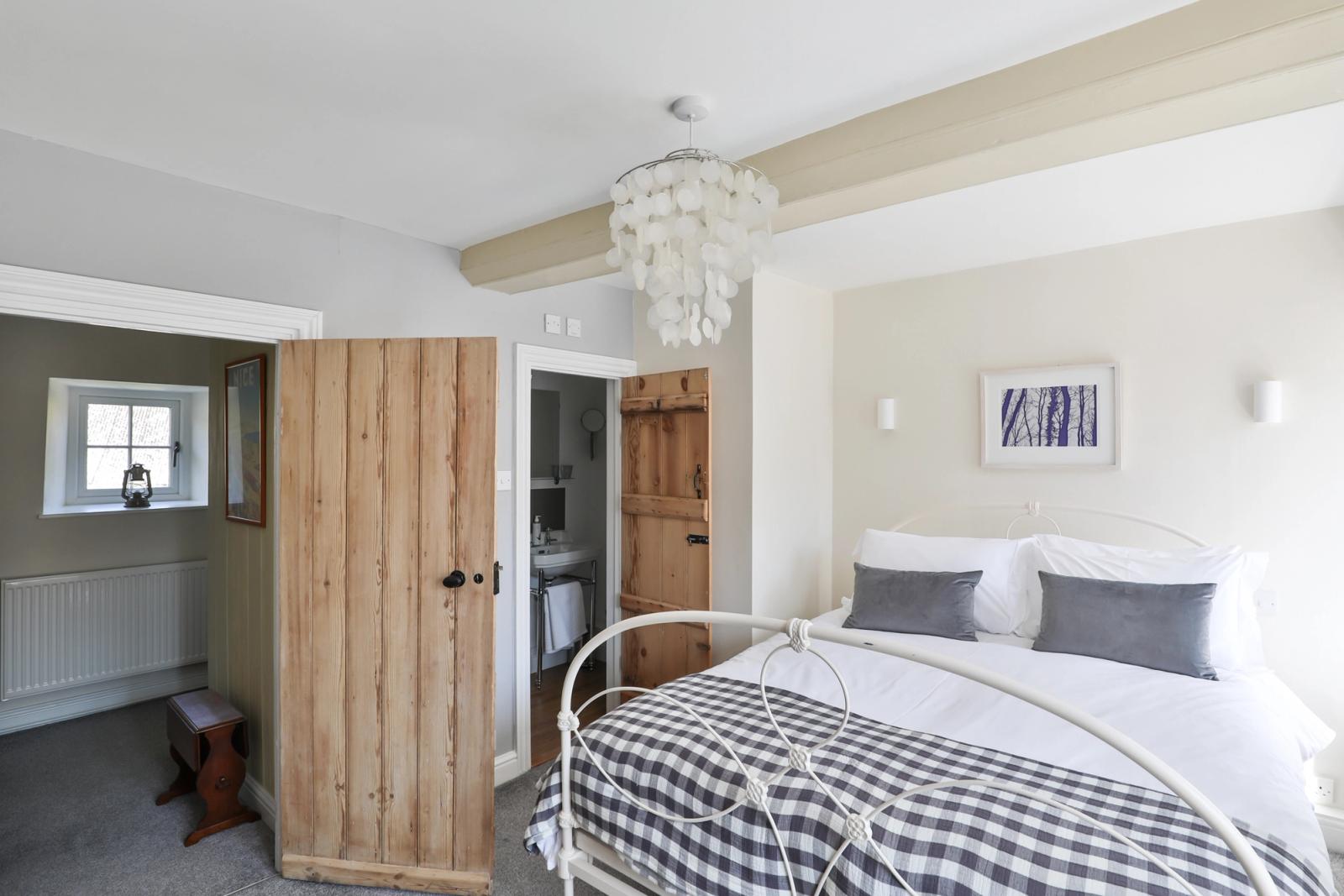 Bedroom with bed, patterned bedding, ensuite bathroom entrance, and cream walls
