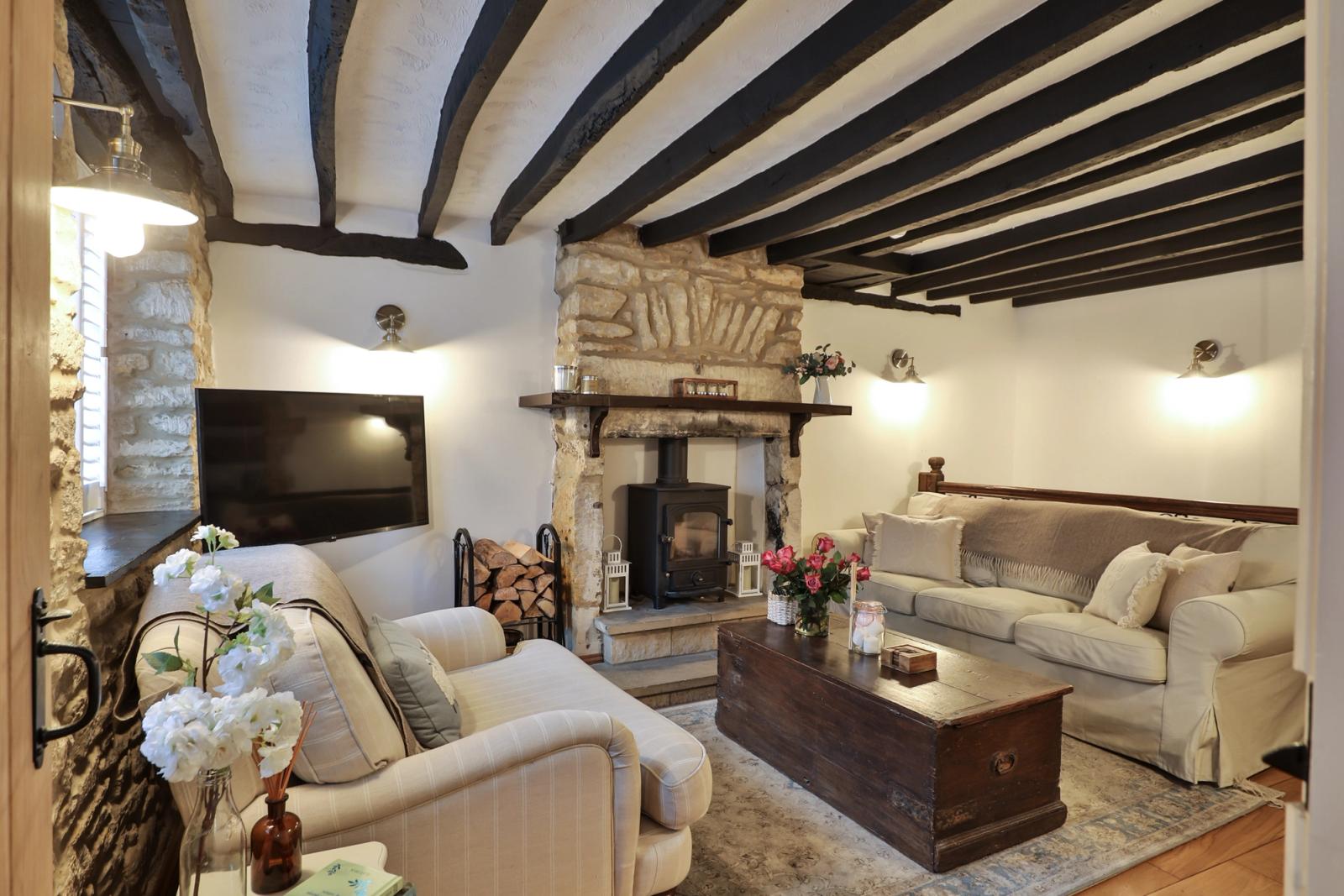 Lounge with exposed dark wooden beams, fireplace, cream seating, and television
