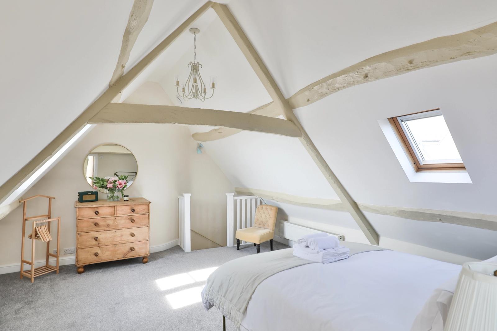 Master bedroom with white bedding, exposed wooden beams, and skylight