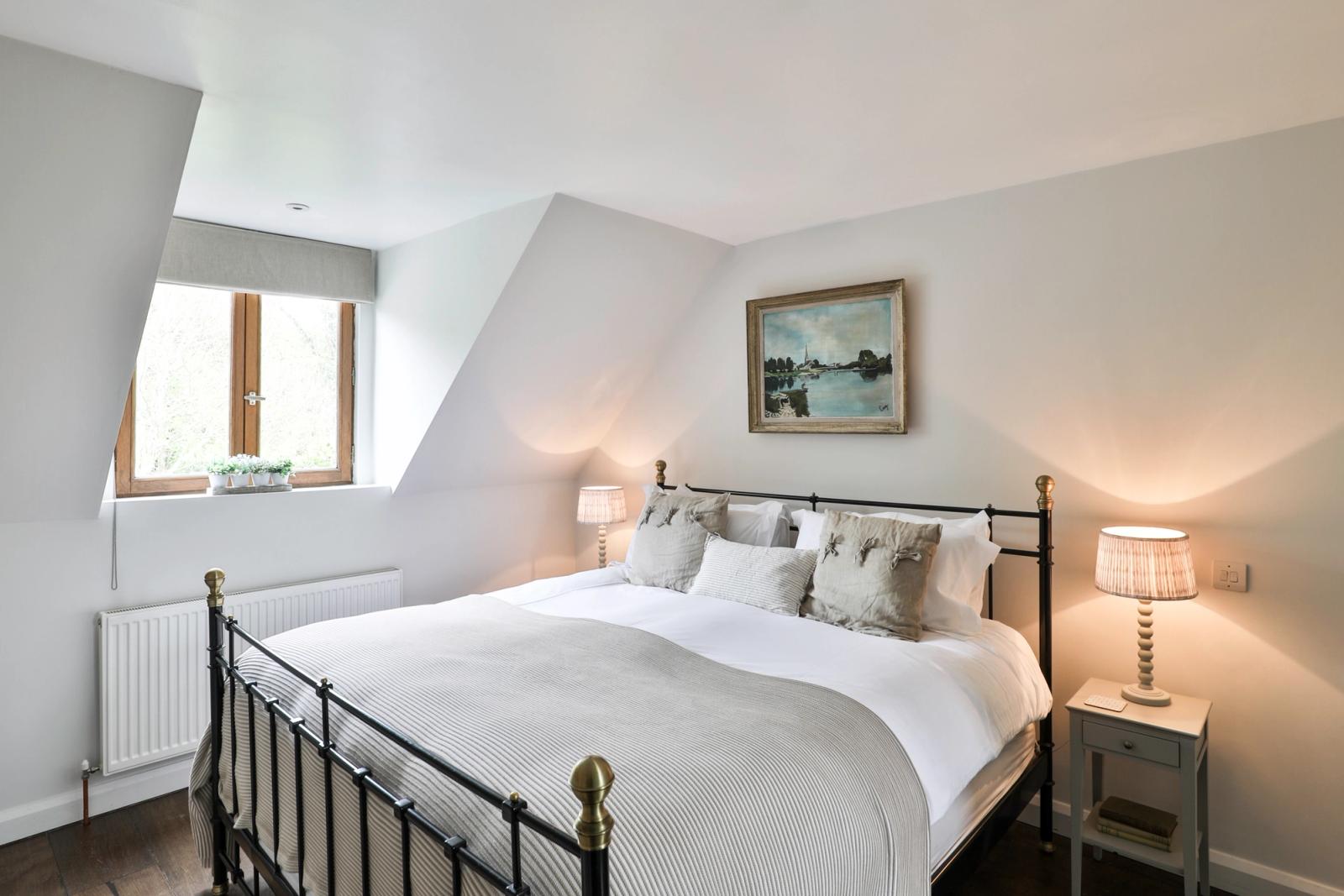 Double bed with white linens, metal headboard, bedside lamps, bedroom window, warm lighting