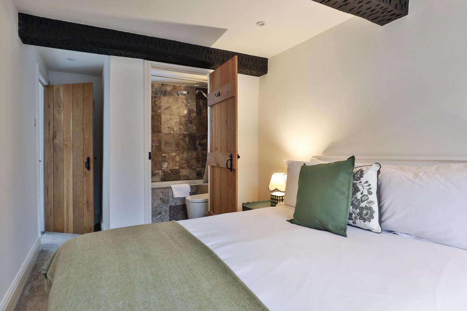 Bedroom with green and white bedding, dark wooden beams, and wooden furniture