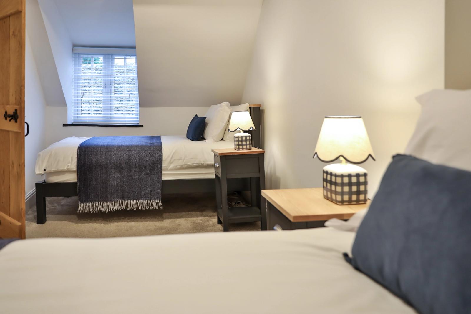 Twin bedroom with two separate beds, sloped ceiling, bedside lamps, and white walls
