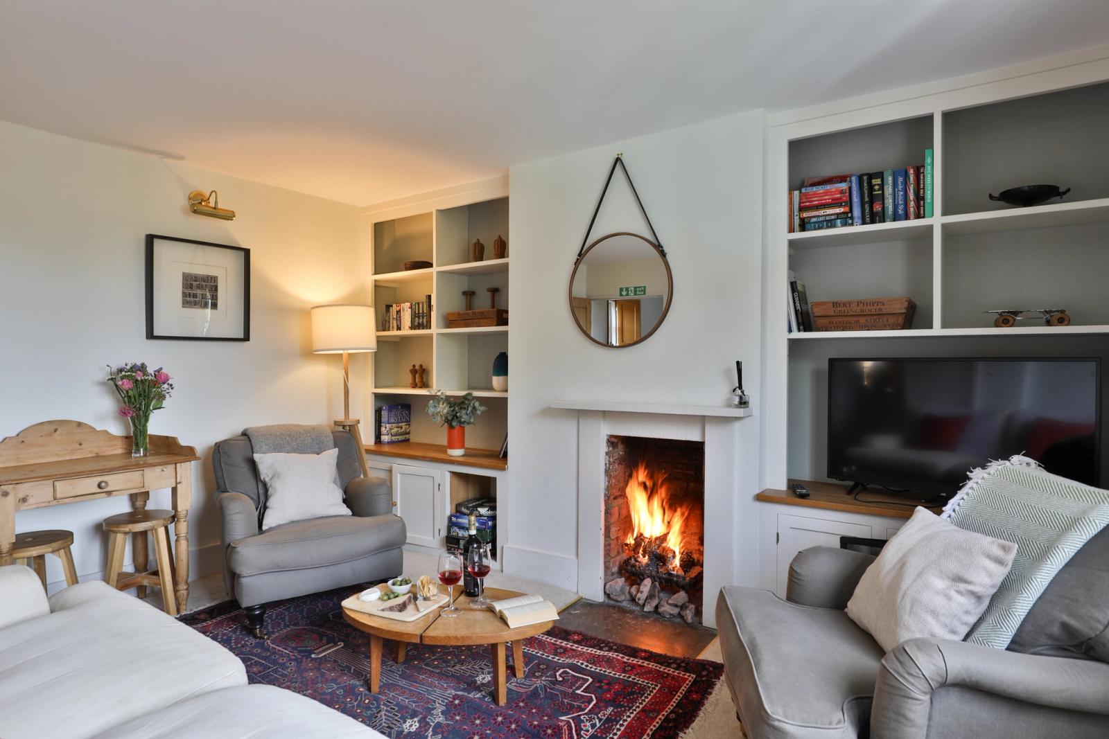 Lounge with lit fireplace, armchairs, shelving, warm lighting, and rug